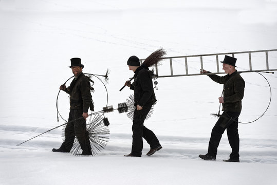 Three chimney sweeps walking in snow