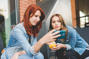 two young women outdoor using smart phone having fun - technology, social network, communication concept