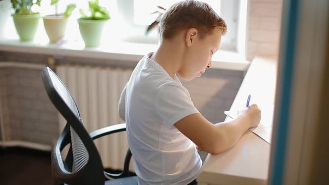 White boy with broken hand doing his hometask of maths sitting at the table. The student is tited , so he warming up his shoulders.