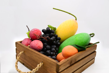 Group of fake fruits in wooden box on white background.  Yellow and green mango, apple, grapes, lychee