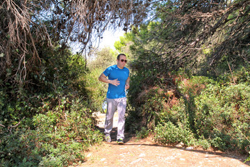 Obraz premium Fit runner man jogging for fitness running at running trail in beautiful landscape nature outdoors. Handsome young sportsmen wearing sportswear and running and exercises in forest. Healthy lifestyle.