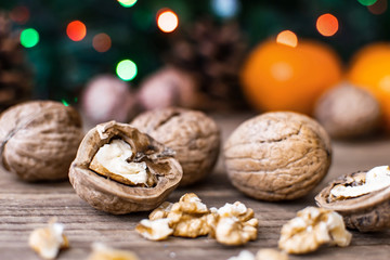 Close-up Walnuts and blurred background with orange mandarines, cones, christmas tree and holiday colored lights on wooden table. Christmas and New Year concept