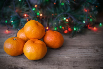 Orange tangerines, christmas tree and holiday colored lights on wooden background. Christmas and New Year card with copy space