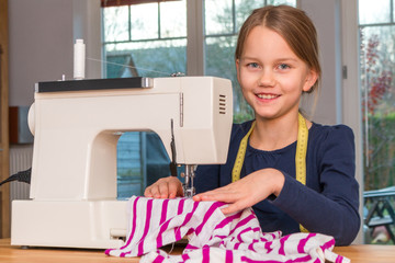 Ein 8 Jahre altes Mädchen näht mit einer Nähmaschine einen gestreiften Stoff zu Hause, Porträt
