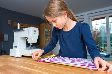 Ein 8 Jahre altes Mädchen mißt mit einem gelben Maßband einen gestreiften Stoff ab, Porträt