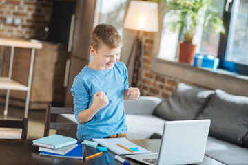 I did it. Cheerful pleasant nice boy smiling and saying yes while finishing his school project