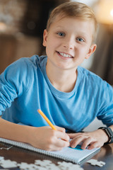 Mind development. Happy positive joyful boy writing in his copybook and smiling while doing his school task