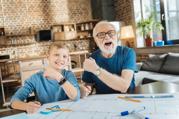 Our watches. Happy positive joyful grandfather and grandson smiling and looking at you while showing their watches