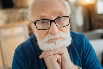 Thoughtful look. Smart nice aged man holding his chin and thinking about life while looking at you