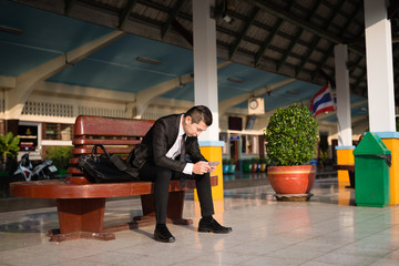 asian Businessman sitting at train station and looking down at mobile phone screen ,Feeling stress about financial crisis and disappoint during working, vintage photo and film style.