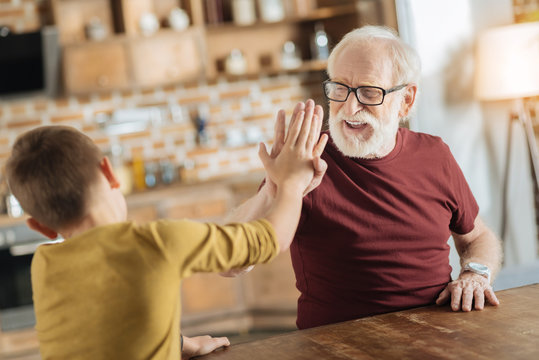 Perfect team. Positive delighted joyful grandfather and grandson smiling and being in a positive mood while giving each other high five