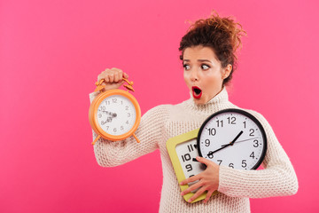 Portrait of a shocked pretty woman holding alarm clocks