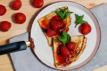 Crepes with fresh strawberries and jam in frying pan