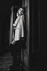 Black and white portrait of young attractive pretty blonde woman in the  jacket, leather shirt, gaiters, patent shoes on the dark background