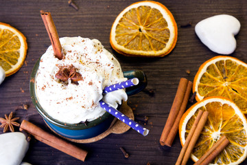 Christmas coffee cup with whipped cream, cinnamon, cocoa powder, anise, dried orange ang gingerbread cookies on wooden table. Dark retro style with copy space.