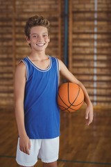 Naklejka premium Smiling high school boy holding a basketball in the court