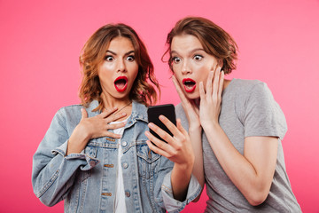 Shocked ladies friends using mobile phone.