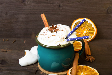 Christmas coffee cup with whipped cream, cinnamon, cocoa powder, anise, dried orange ang gingerbread cookies on wooden table. Dark retro style with copy space.