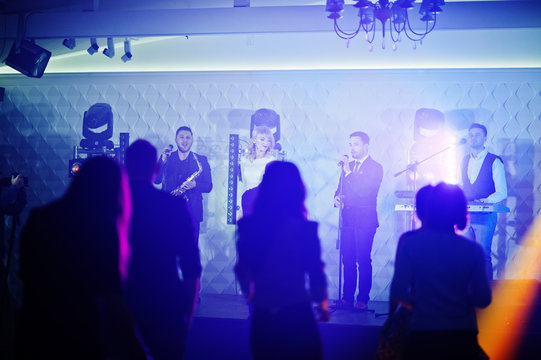 Musicial music live band performing on a stage with different lights with crowd of people fans.