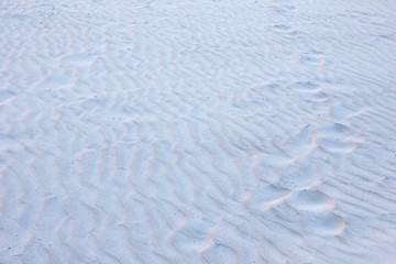 Human footprints of bare feet on textured sand, snow