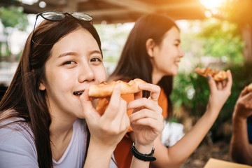 Asian students eating eating the pizza together in breaking time early next study class having fun and enjoy party, Italian food slice with cheese delicious at university outdoor.