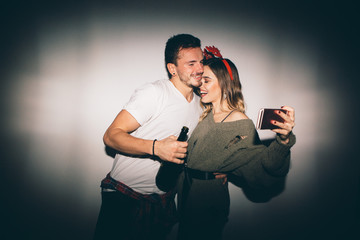 New Year's Party. Girl and boy posing in front of white wall and taking selfie 
