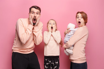 Surprised young family looking at camera on pink