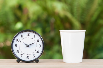 Coffee mug and alarm clock on wooden table.