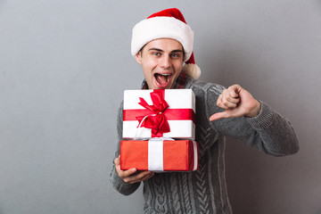 Funny man in sweater and christmas hat holding gifts