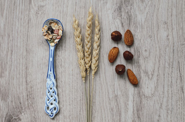Fototapeta na wymiar Muesli with nuts hazelnuts, almonds, porcelain spoon and wheat ear. Muesli on a wooden table. Muesli top view. Healthy food