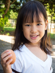 Cute Asian girl holding egg in hand. Showing egg and smiling. Concept of food ingredient for hi nutrition best for child.