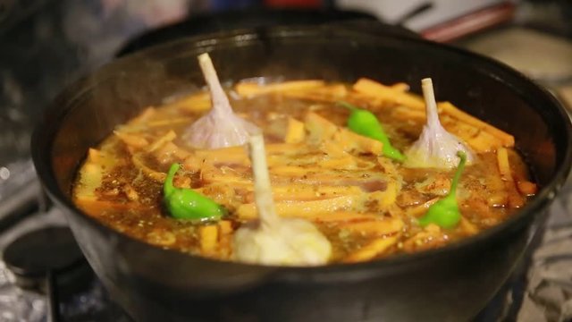 Cooking pilaf, shef adds garlic and green chili peppers into a cast-iron kettle