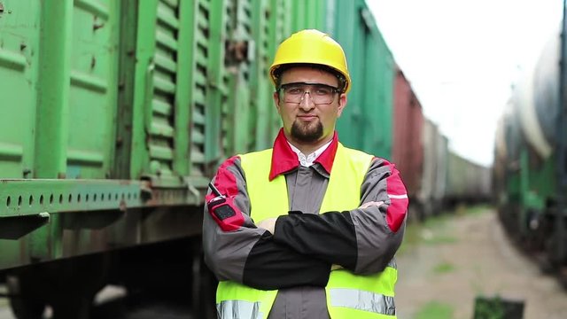 Railway worker looks at the camera. Railwayman stands between goods trains on freight station