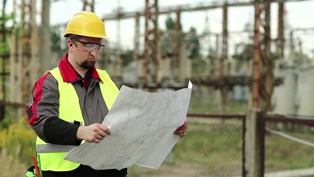 Powerman with scheme of works on power station. Worker with construction documentation at power plant. Master builder in hard hat and with design drawings