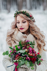 A young girl of Slavic appearance with a wreath of wildflowers. Beautiful bride holds a bouquet in winter background.