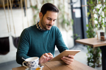 Handsome man smiling and holding tablet computer in coffee shop