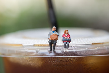 Male and female miniature figures with hand bag sitting and waiting on top of plastic take away cup...