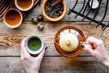 Pour tea from tea pot. Cups, dry tea leaves on rustic wooden background top view