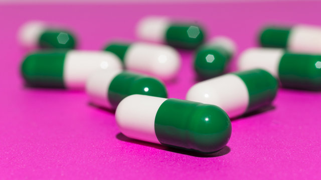 Heap of white and green capsules on purple background.