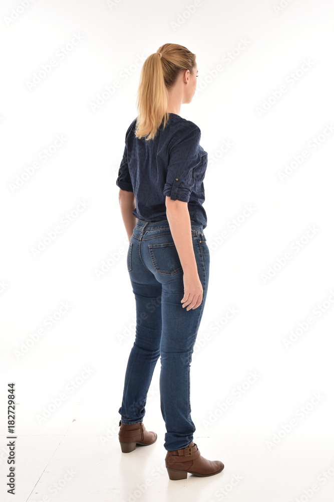 Poster Full length portrait of a girl wearing simple blue shirt and jeans, standing pose facing away on a white background.