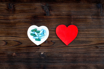 Treat heart. Pills in bowl in shape of heart on dark wooden background top view copyspace
