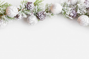 Christmas frame with fir tree branches with snow, balls ornaments and cones with copy space, festive greeting, top view