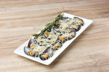 Fried mussels in the sink on a plate. Mussels in a sauce and grated Parmesan in a plate on a wooden table.