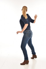 Full length portrait of a girl wearing simple blue shirt and jeans, standing pose facing away on a white background.