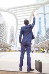 Businessman raising his fist  in the air, with office building background - business success, achievement, and win concepts