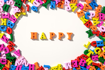 The word Happy is lined with colourful wooden letters on a white table with scattered in a circle with letters