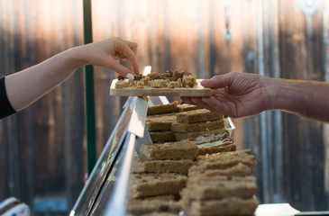 Woman selecting flapjack sample from market stall selling cakes and other baked food