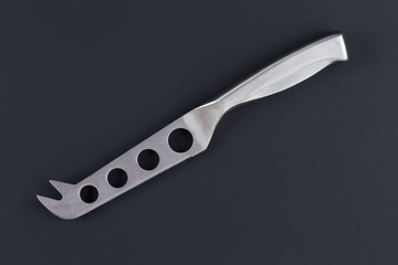 A special kitchen knife for cheese on a dark surface with a soft shadow.
