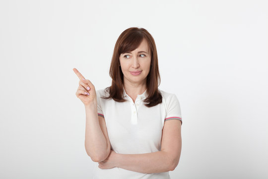Smiling middle aged woman wearing blank white t-shirt showing something by her finger, mock up on white background.