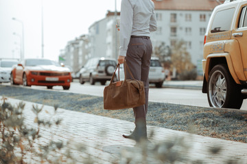 Cool man beautiful model outdoors, city style fashion. A handsome man model walking in the city center next to some cars. urban setting. The young boy as trendy, modern clothing with bag